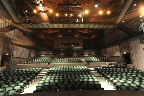 The view from the stage of a large and impressive proscenium theatre with deep green upholstered seats.