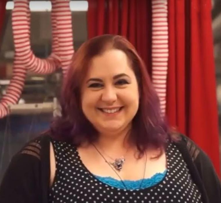 Danee Gosselin is shown in the costume shop smiling warmly with fabric pieces and sewn objects in the background.