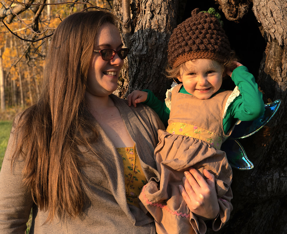  Jessie Chapman is shown outdoors dressed for autumn holding her toddler daughter in one arm.  Both are smiling.