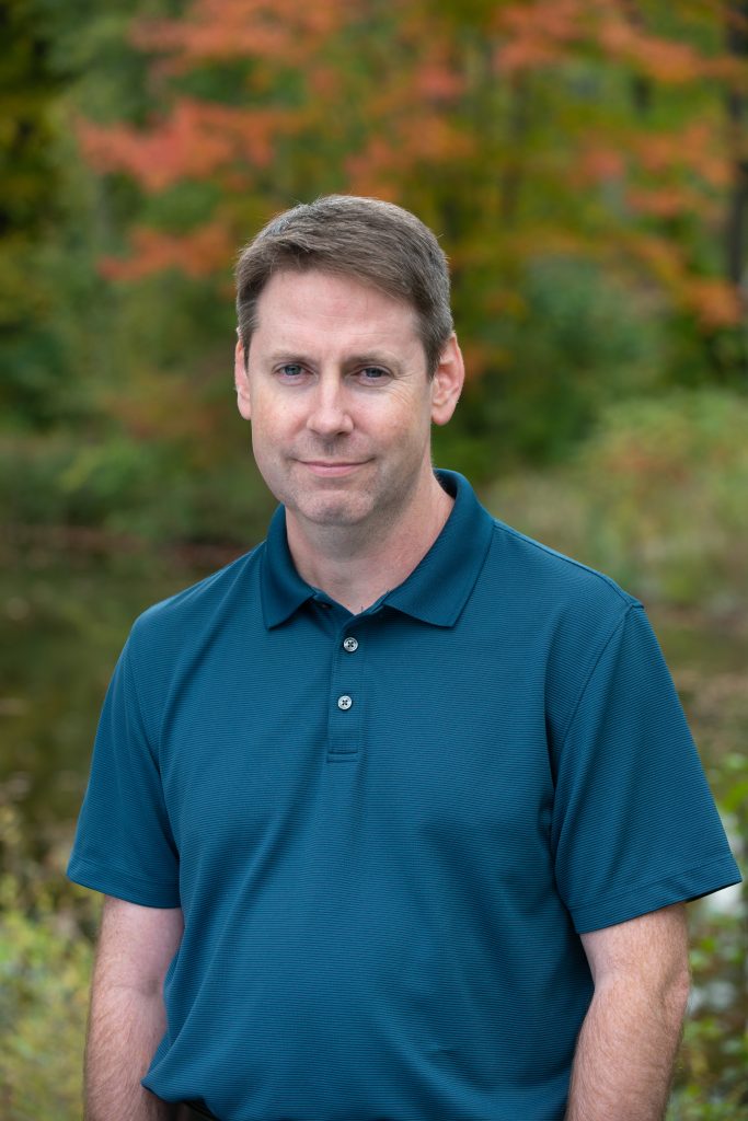 Justin McCarthy is shown outdoors wearing a blue polo smiling.