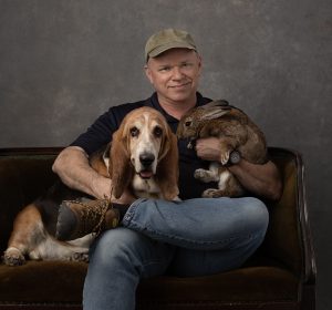 Matt Kizer photographed with two of his pets, a basset hound and a rabbit.