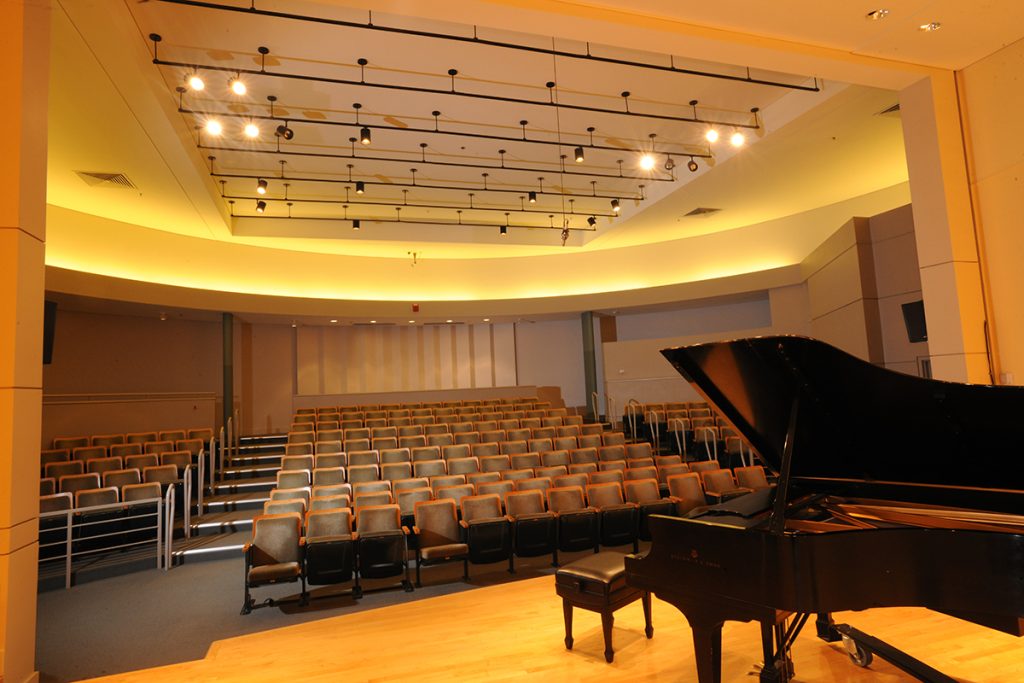 A beautiful music hall with formal seating and a grand piano on the stage.